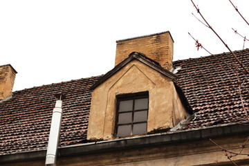 Vintage attic window on red tile roof with chimney