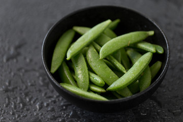 vegetable, food and culinary concept - close up of peas in bowl on wet slate stone background