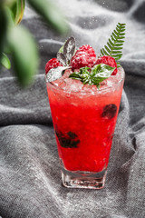 Glass with strawberry mojito cocktail with lemon and mint, cold refreshing drink or beverage with ice on gray background. Overhead view, copy space. Advertising for cafe menu. Vertical photo.