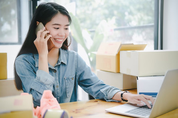 Beautiful young asian business owner working with computer and tablet standing in workshop.Responding on business e-mail,writing the order of product customer orders.