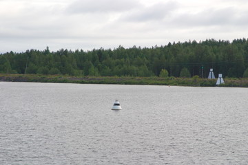 Image of a white sea buoy on the water and navigation sign on the shore