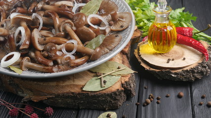 Pickled forest mushrooms in a plate on a black wooden table with butter and spices