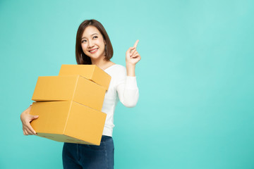 Happy Asian woman holding package parcel box and pointing finger to empty copy space isolated on...