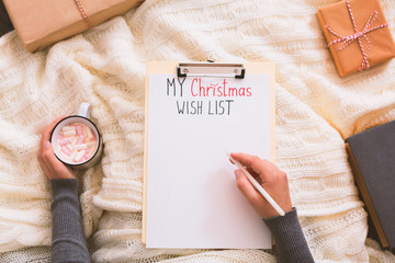 Woman writing with pen on clipboard and drinking hot cocoa
