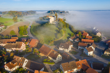 Aerial view of warm sunrise over a typical foggy Swiss medieval town Waltalingen. Hilltop Castle...