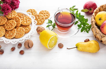 Tea with herbs fruits and cookies. Still life with hot drink apple and nuts at white wooden board in rustic style.