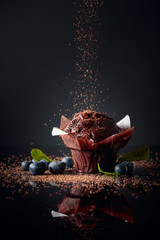 Chocolate muffin sprinkled with chocolate crumbs on a black reflective background. Muffin with berries and mint. - obrazy, fototapety, plakaty