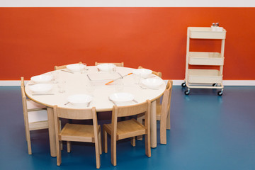 table and chairs in a kindergarten, minimal set up with white plates with a reddish background and blue floor
