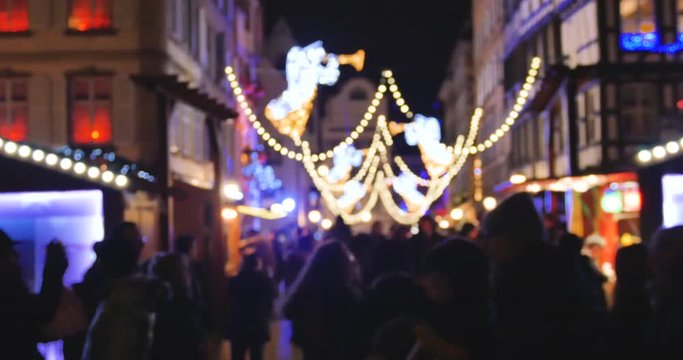 Large group of people pedestrians walking between the Christmas chalets market stalls during annual Christmas Market shopping gifts mulled wine sweets souvenirs defocused blurred silhouettes