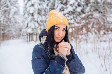 Fototapeta na wymiar Portrait of a brunette woman in a yellow hat on a background of a winter forest. Closeup portrait of a girl in a snowy park.
