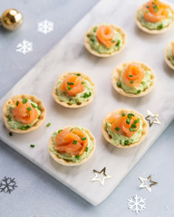 Canapes with smoked salmon, cream cheese and avocado on light background with space for text. Christmas and new year holidays background concept. Starters snacks recipe ideas. Top view.