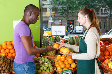 Obraz premium Seller woman is helping man choose fresh oranges in the fruit market.