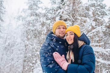 Obraz premium young couple in love walks in the winter forest. active winter holidays. A couple hugs and laughs on a background of a snowy forest. Closeup portrait of a guy and a girl in a snowy forest.