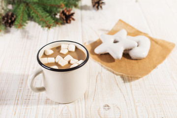 Obraz na płótnie Canvas Hot Christmas drink with marshmallows in an iron mug and gingerbread cookies, on a white table.