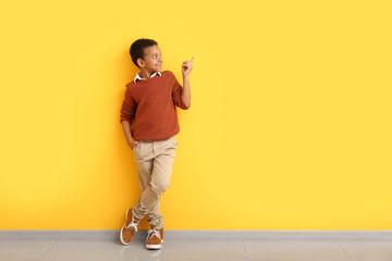 Fashionable African-American boy in autumn clothes pointing at something while standing near color wall