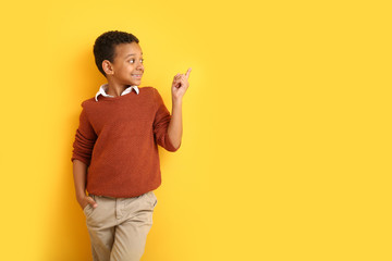 Fashionable African-American boy in autumn clothes pointing at something on color background