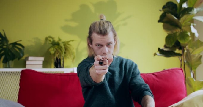 Portrait of young serious millennial man pointing finger at camera like blaming someone staying indoors at home living room.