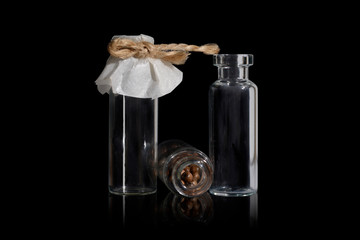 Three small glass vial with brown pills on the black. Vials are tied with twine. 