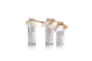 Three small glass vials of white pills tied with twine. On white background.