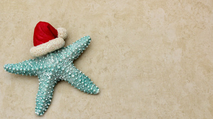 turquoise starfish wearing Santa hat close up isolated on a festive tan sandy background with copy space