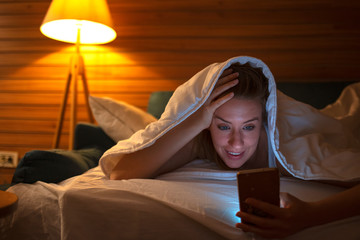 Shot of a young woman using a cellphone in bed at night. Those conversations that last for hours. Female using smartphone / notebook in bed at night. Young beautiful woman having late night video call