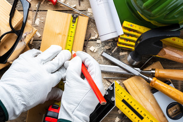 View from above. Carpenter wears protective leather gloves, with pencil and meter marks the measurement on a wooden board. Construction industry, do it yourself. Wooden work table.