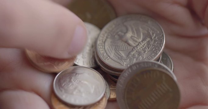 Detail of Caucasian woman's finger sorting through a hand full of assorted United States coins with heads and tails up. Macro close-up with shallow focus and soft daylight lighting, recorded at 60fps 