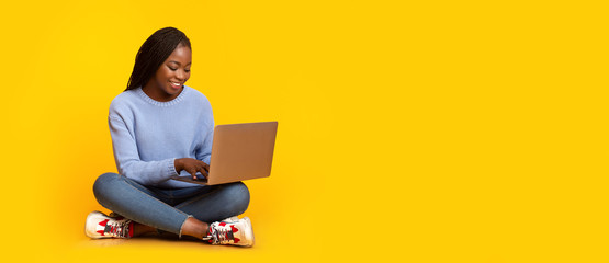 Smiling black girl using laptop over yellow background