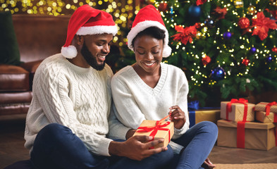 Obraz na płótnie Canvas Black couple celebrating Christmas at home, unwrapping presents together