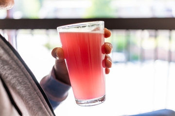 Man sitting outside holding drinking glass of red pink lemonade cocktail juice closeup of drink...