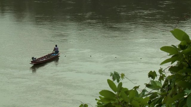 Fisherman in small boat paddling and maneuvering towards a line of white buoys
