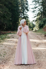 Beautiful elegant bride with hijab in nude pink dress with long full skirt and long sleeves. Outdoors, on te road. She is posing for fashion clothes. 