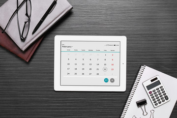 Flat lay composition of tablet with calendar app on black wooden table
