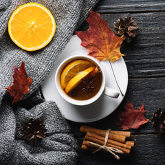 Mug of hot tea composition with orange, cinnamon and anise on the table with knitted warm sweater and dry red maple leaves top view