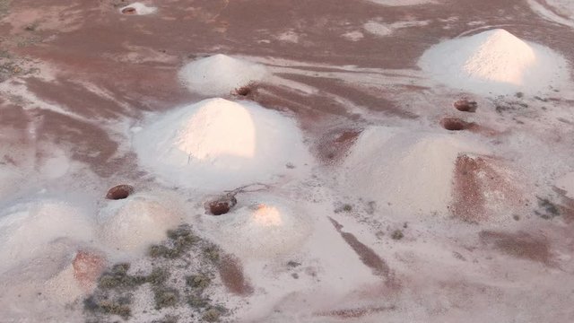 Aerial: Working Opal mine in the outback region of Coober Pedy at sunrise. Heaps of mining sand visible in piles from excavated holes. Australia