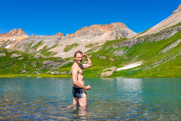 Young fit man flexing standing in cold colorful water of Ice Lake on famous trail in Silverton, Colorado in San Juan Mountains in summer swimming