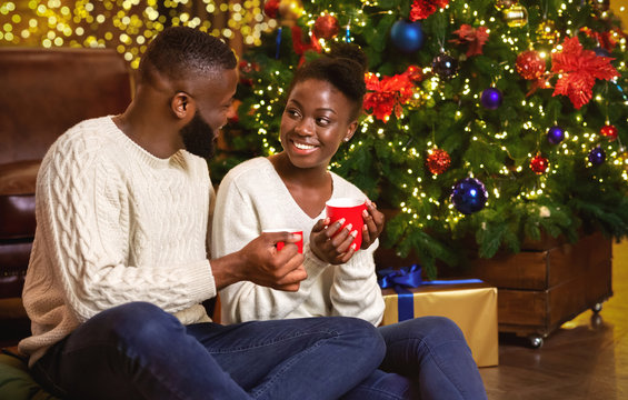 Romantic african american couple drinking hot chocolate near Christmas tree