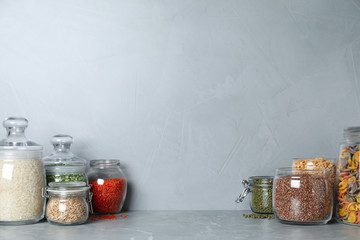 Glass jars with different types of groats on grey marble table