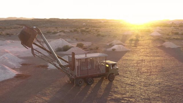 Aerial: Opal vacuum mine truck in a working mine in the outback region of Coober Pedy at sunrise. Heaps of mining sand visible in piles from excavated holes. Australia