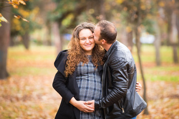 Happy pregnant couple kissing  in autumn background