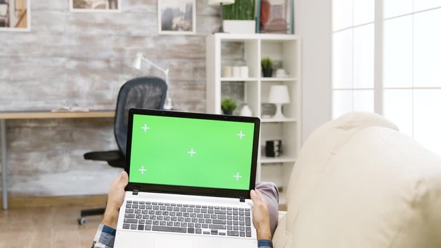 Man lying on the sofa and holding a green screen laptop