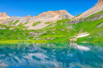 Landscape view of green grass meadow and Ice lake water reflection near Silverton, Colorado in August 2019 summer on summit with snow