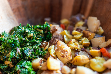 Macro closeup of wooden bowl of vegan food with green kale salad and roasted potatoes with zucchini...