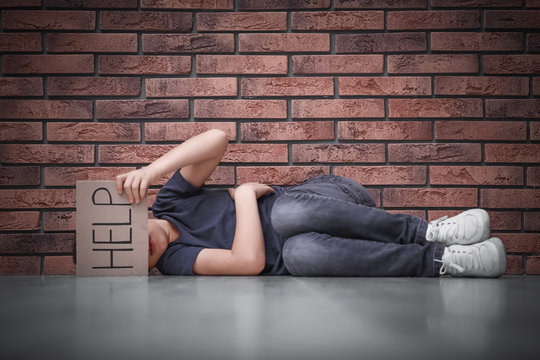 Little boy with sign HELP lying on floor near brick wall. Child in danger