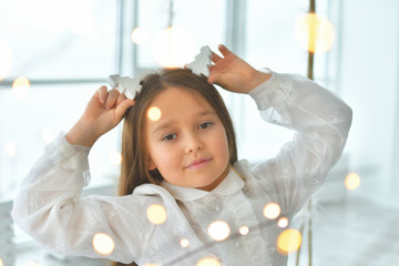 Cute long-haired girl in a white retro dress makes a wish for new year. Happy little girl excited...