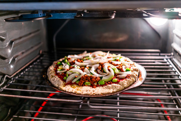 Inside oven with rack and homemade pizza cooking baking with tomato sauce, toppings green bell...