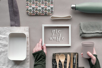 Frame with text "Zero waste", top view, creative green concept of lunch kit. Flat lay, eco friendly takeaway lunch set - bamboo cutlery, lunch box, cotton bag and hand with coffee cup on craft paper.