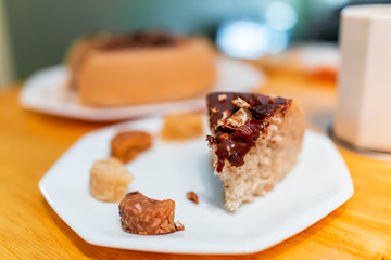 One slice closeup of yellow vanilla homemade sponge cake with chocolate frosting and coconut macaroons on table and bokeh background of dessert
