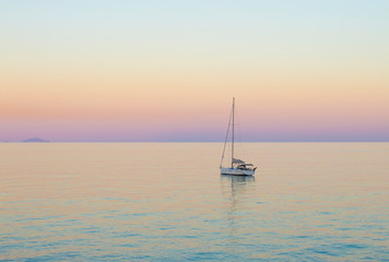 Naklejka premium Small white sailboat in Aegean sea by Greek island of Santorini in calm summer evening after sunset.