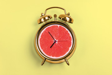 Yellow Alarm Clock With Blood Orange- Time Concept and light yellow background